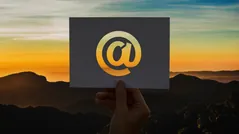 Hand holding a card with an @ symbol against a sunset mountain landscape representing email marketing