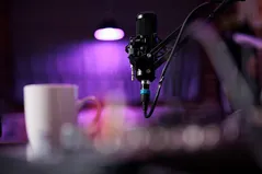 Podcast microphone on a boom arm beside a coffee mug in a purple-lit studio