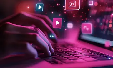 Person typing on a laptop with glowing video, email and play icons representing content marketing